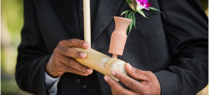 Groom with cannabis boutonniere holding a cannabis pipe at wedding