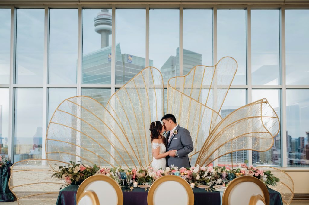 Bride and Groom kissing in front of gold wings in front of window and CN Tower 