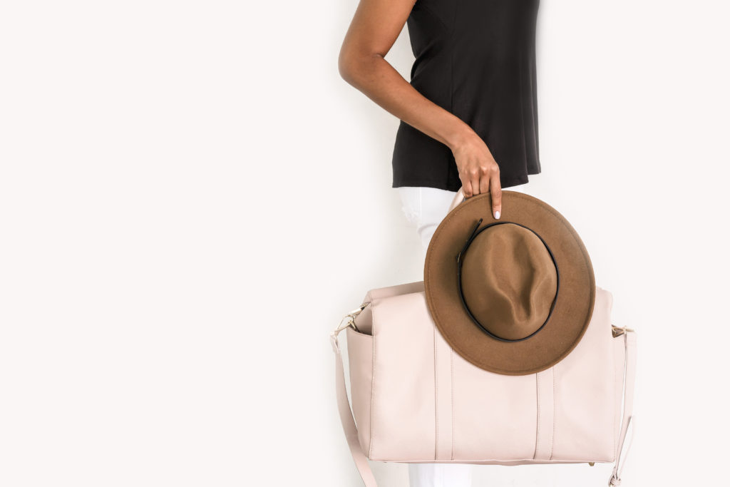 Woman with carryon bag and hat, ready to travel.